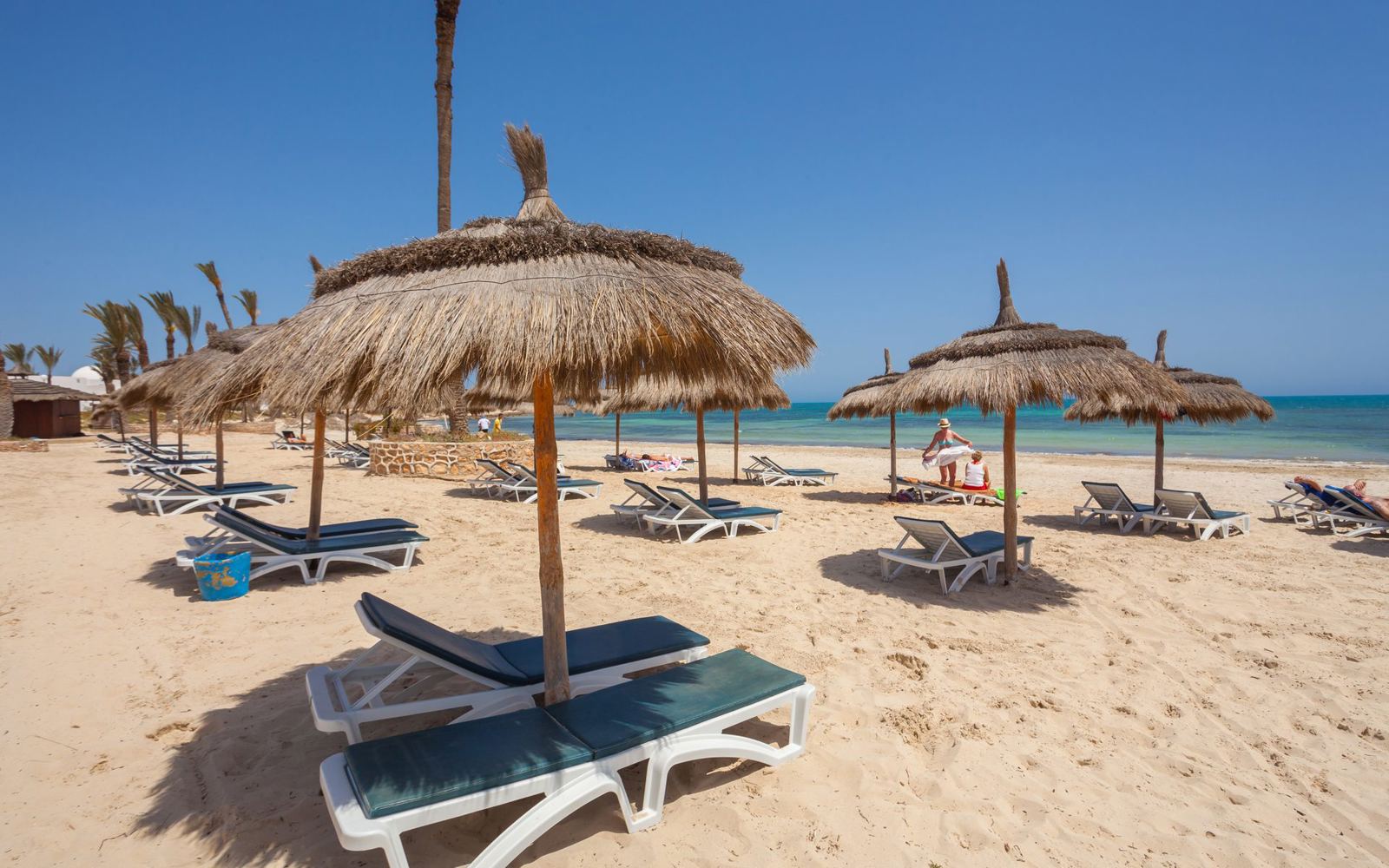 Thatched parasols and sun loungers on the beach at Djerba - Sunshine4u